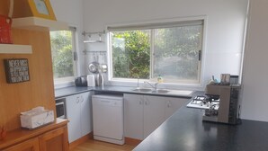 A modern kitchen with white cabinets, a dishwasher, a coffee machine, and a window with a view of greenery. - 11A Seaview. 
Ocean and Otway Ranges views. Close to beach. Pet friendly. (Apollo Bay)