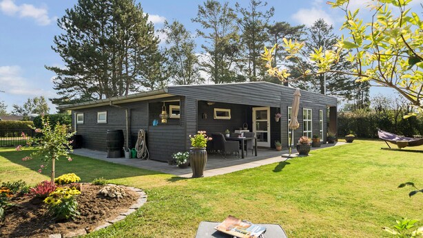 Una casa moderna de dos pisos con un patio, mobiliario exterior y un jardín.
