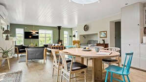 Una sala de estar amplia con chimenea, un comedor con mesa redonda y una cocina a la vista al fondo.