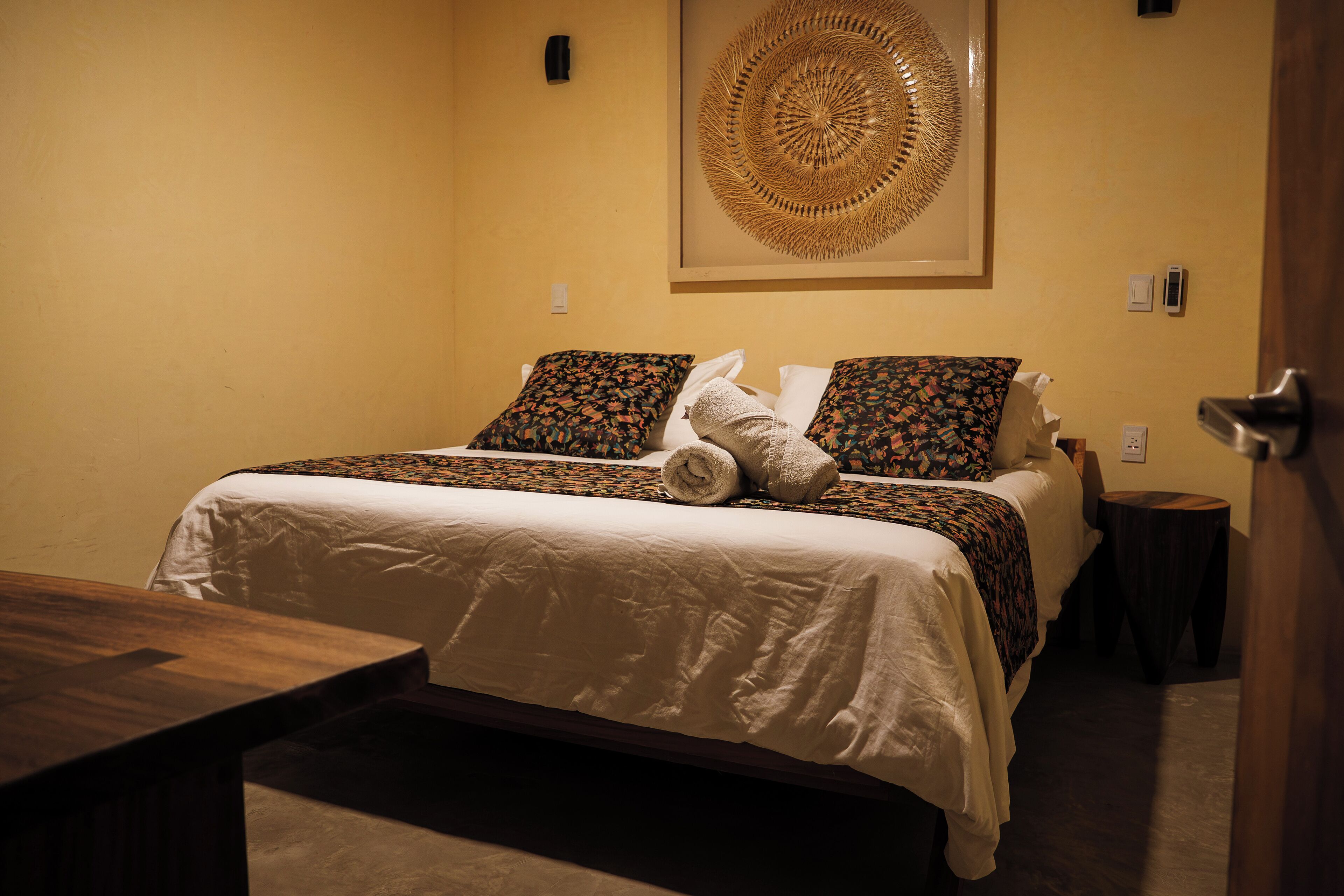 Camera d'albergo con un letto, cuscini, una coperta, un comodino in legno e un'opera d'arte appesa al muro.