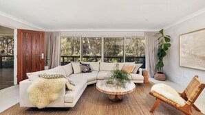 Ein stilvolles Wohnzimmer mit Ecksofa, rundem Couchtisch und einem Rattan-Sessel.