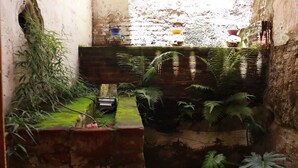 Un patio estrecho con un muro de ladrillo, un pequeño banco de madera y diversas plantas en macetas.