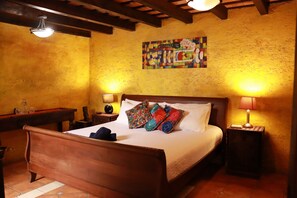 A bedroom with a wooden bed, two bedside tables with lamps, a colorful abstract painting on the wall, and a tiled floor. - Casa Quetzalli Centro Historico (Antigua Guatemala)