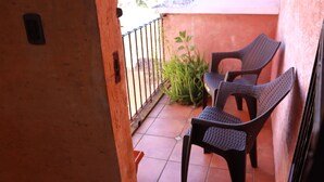 Un pequeño espacio al aire libre con dos sillas, una mesa, barandal de metal y una planta en maceta.