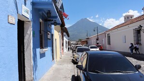 Una calle estrecha bordeada de edificios coloridos, coches aparcados y una montaña al fondo.