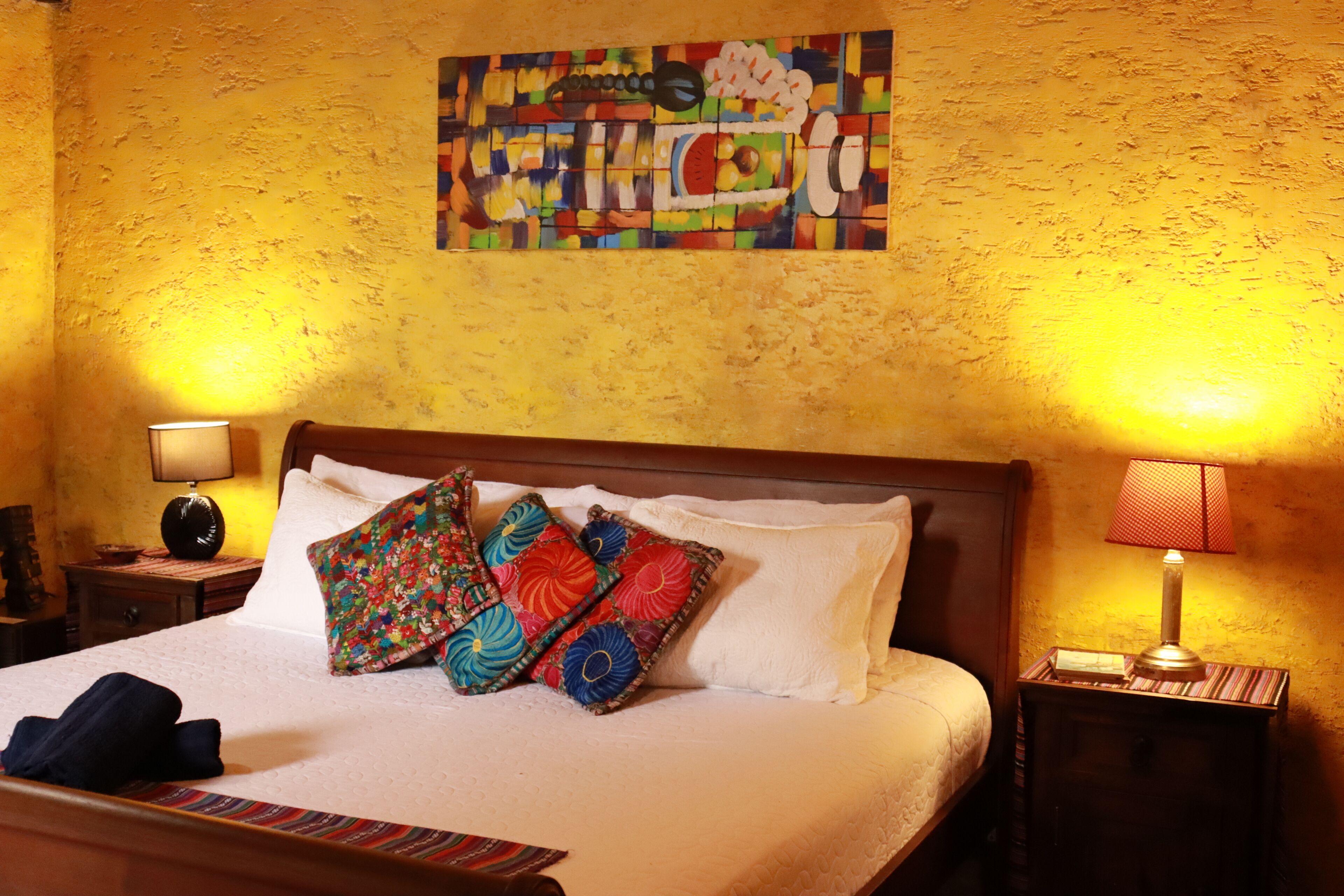 A hotel room with a bed, pillows, a nightstand, and a wall painting.
