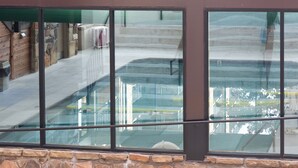 Blick durch ein Fenster mit einer Stein-Fassade, einem Metallgeländer und einem Gebäude-Spiegelbild mit Treppe und Pool.