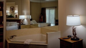 Ein Hotelbad mit Badewanne, Spiegel, Nachttisch mit Lampe und einem gerahmten Bild an der Wand.