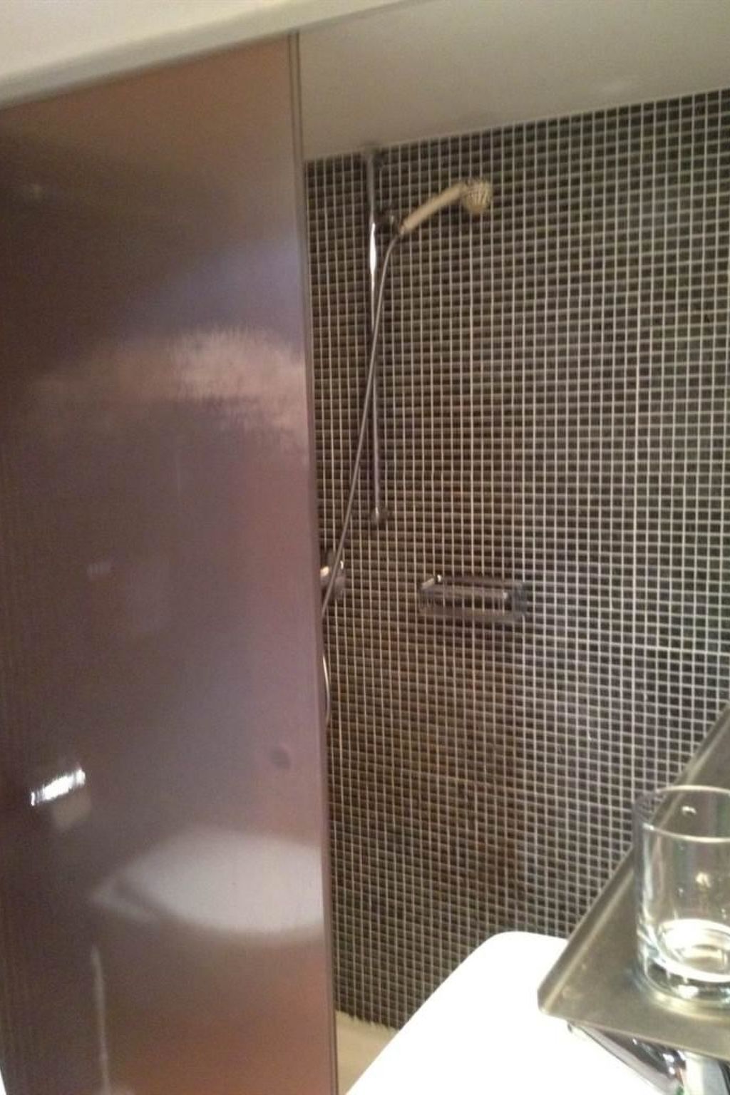 A bathroom with a shower, a glass of water, and a tiled wall.