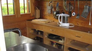 Een keuken met een roestvrijstalen spoelbak, houten keukenkastjes en verschillende keukengerei dat aan de muur hangt.