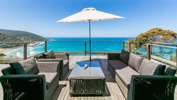 A deck with wicker furniture, a glass-top table, and a white umbrella overlooking a coastal view. - Arguably the best views in Wye River (Wye River)