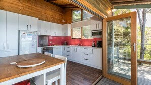 A modern kitchen with white cabinets, a red tiled backsplash, and a wooden dining table. - Arguably the best views in Wye River (Wye River)
