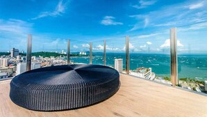 Een modern, rond zwart zitgedeelte op een dak, met een panoramisch uitzicht over de stad en de oceaan.