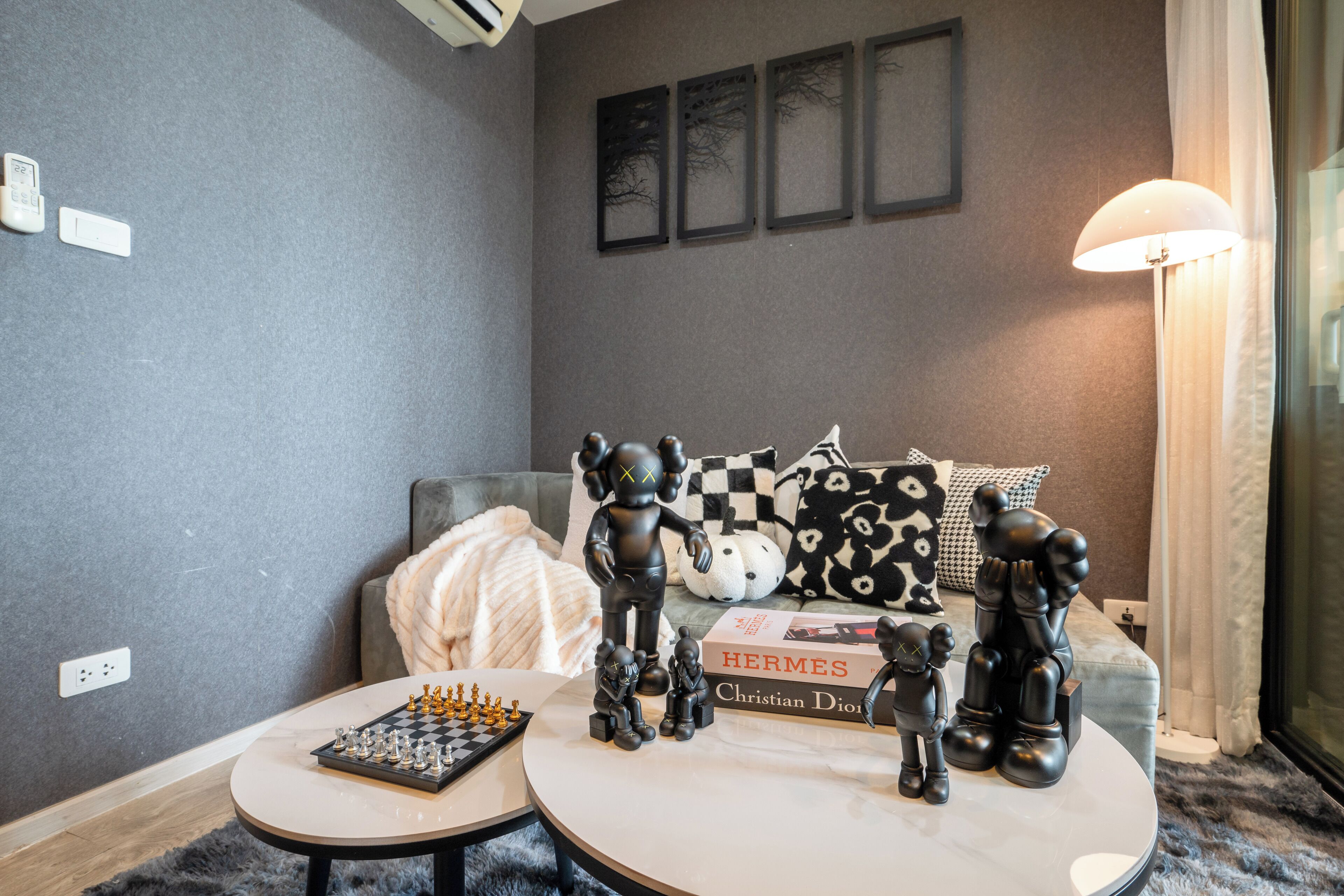 A living room with a chessboard, a book titled 'HERMES Christian Dior', and decorative figurines on a round table.