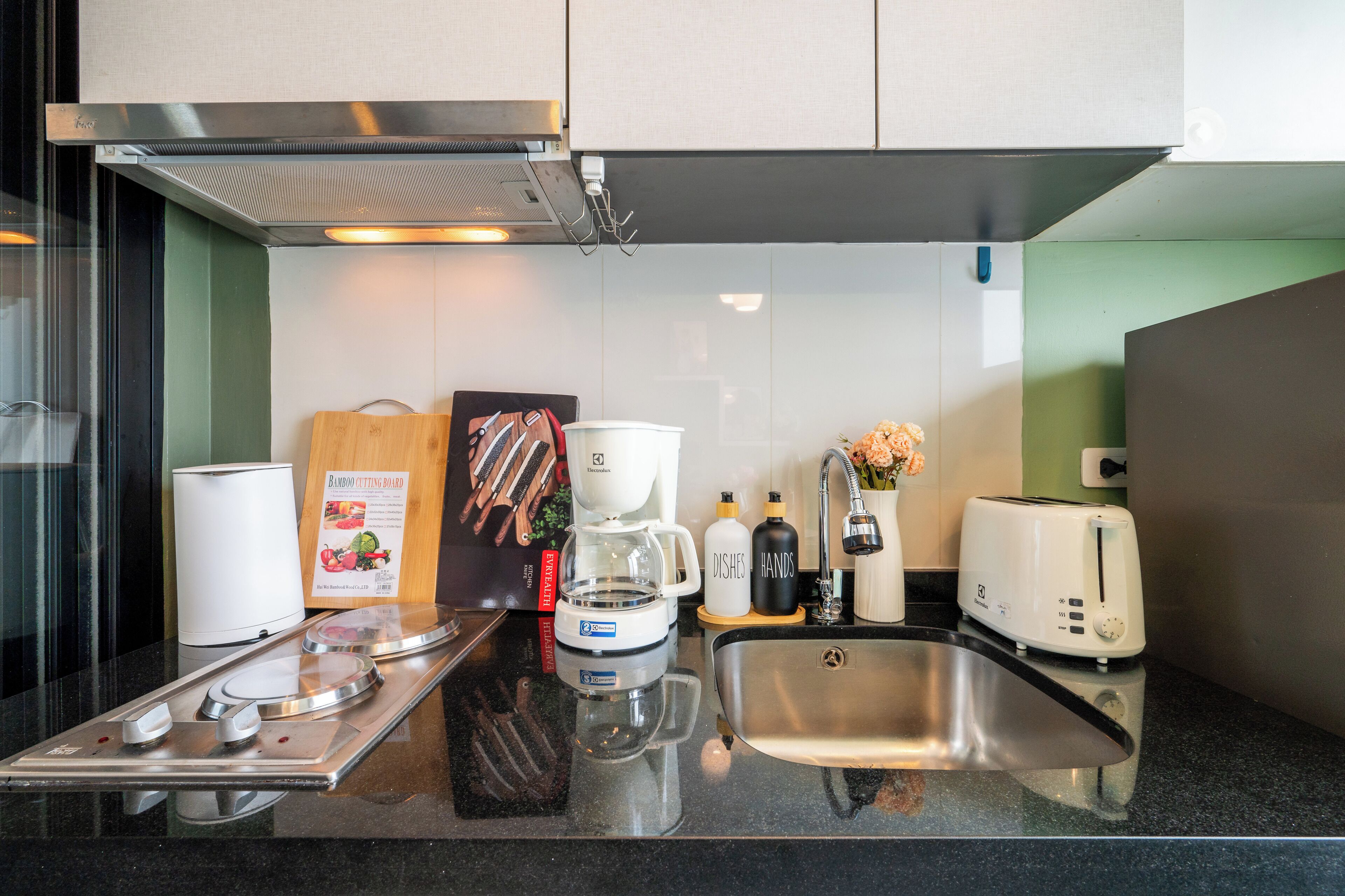 A modern kitchen with a stainless steel sink, a coffee maker, a toaster, and a bamboo cutting board.