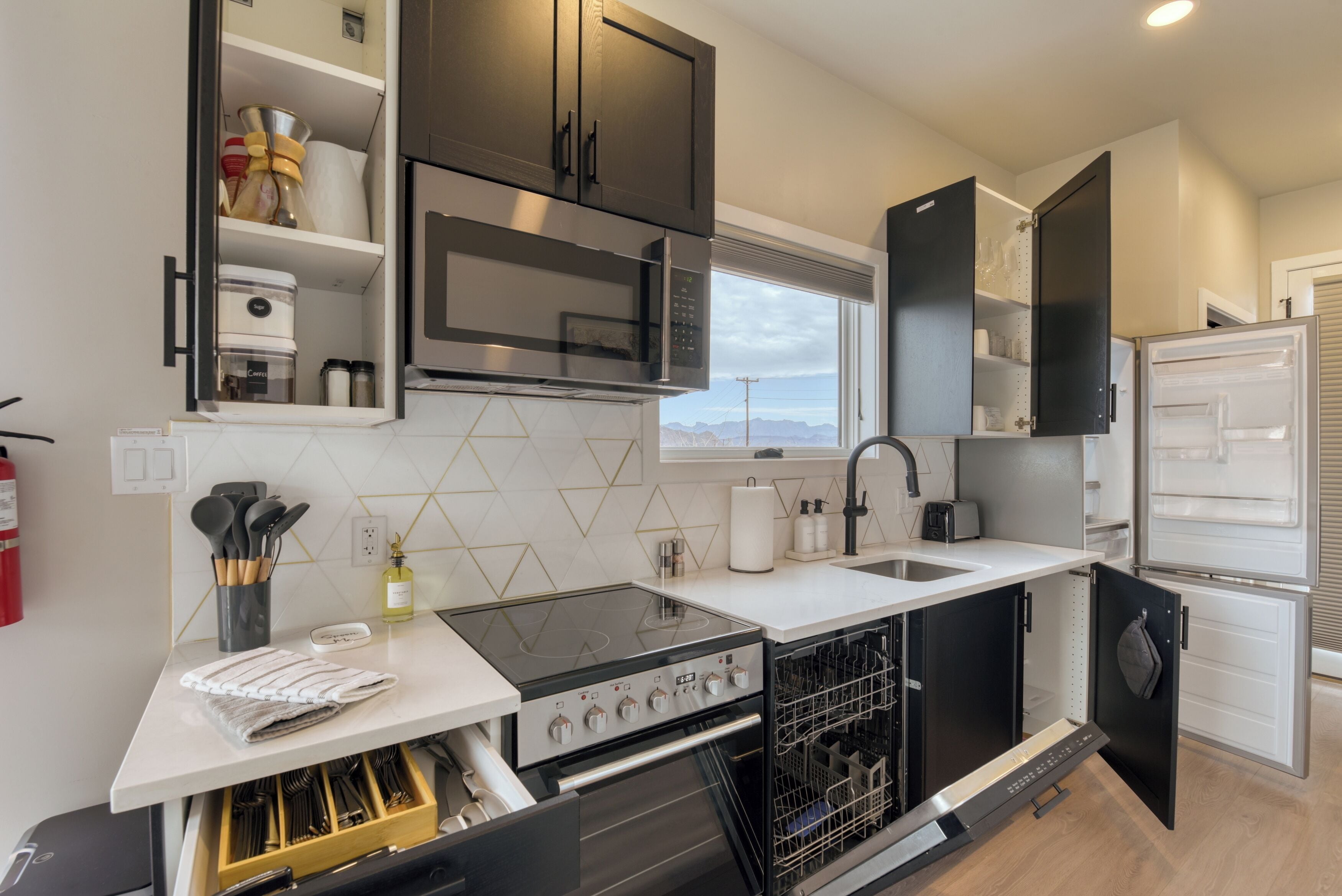 A modern kitchen with black cabinets, a stainless steel stove, and a built-in dishwasher.