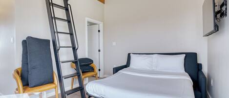 A bedroom with a bed, a chair, a ladder, and a TV mounted on the wall.