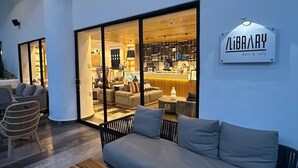 Un intérieur moderne avec un espace salon, un comptoir bien visible et une enseigne indiquant « LIBRARY, épicerie-traiteur et café ».