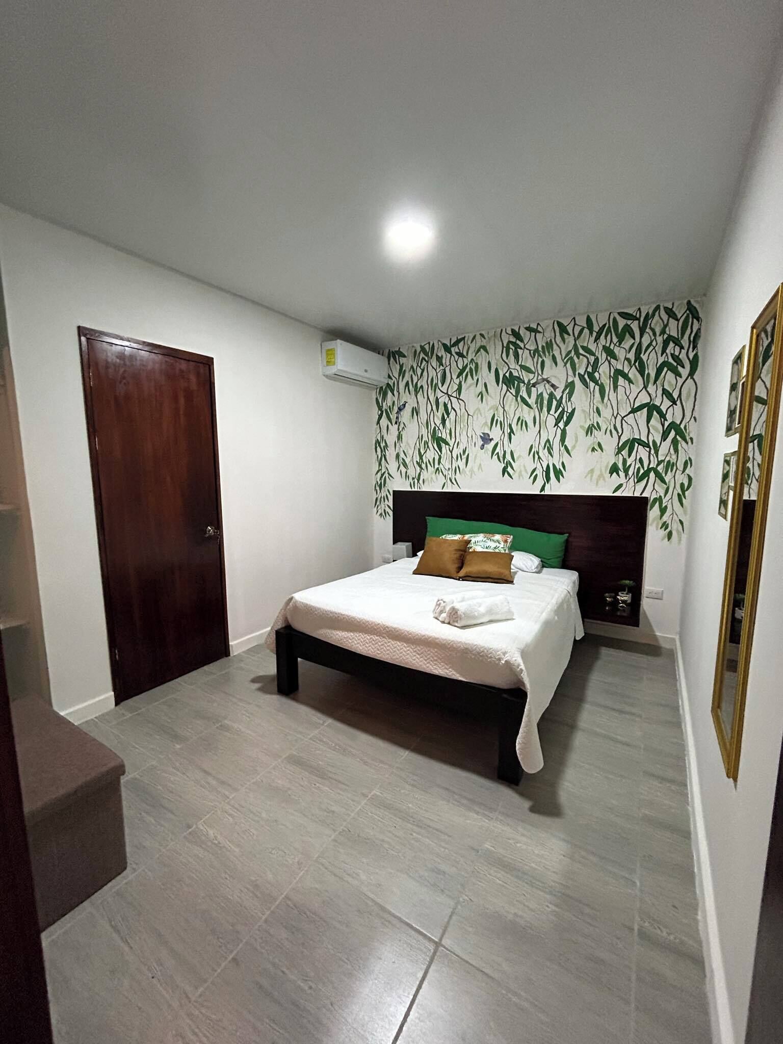 A bedroom with a bed, a wooden door, a wall-mounted air conditioner, and a patterned wallpaper.