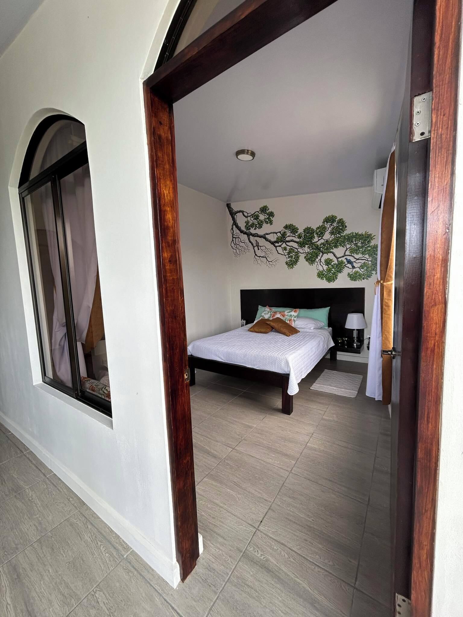 Een slaapkamer met een bed, een nachtkastje, een lamp en een kunstwerk aan de muur.