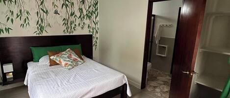 Una camera da letto con un letto, un comodino, una parete con motivo a foglia e una porta che conduce in un'altra stanza.