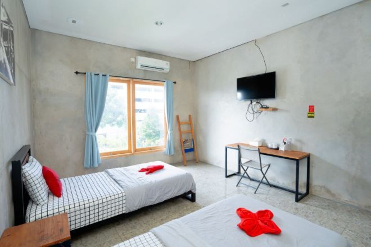 A room with two beds, a desk, a TV, and an air conditioning unit.