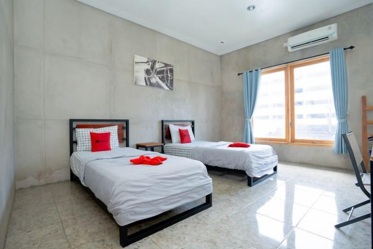 Habitación de hotel con dos camas, un ventanal con cortinas, un cuadro en la pared y un equipo de aire acondicionado.