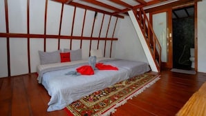 Un dormitorio con techo inclinado, vigas de madera, una cama con alfombra estampada y una escalera que lleva a un baño.