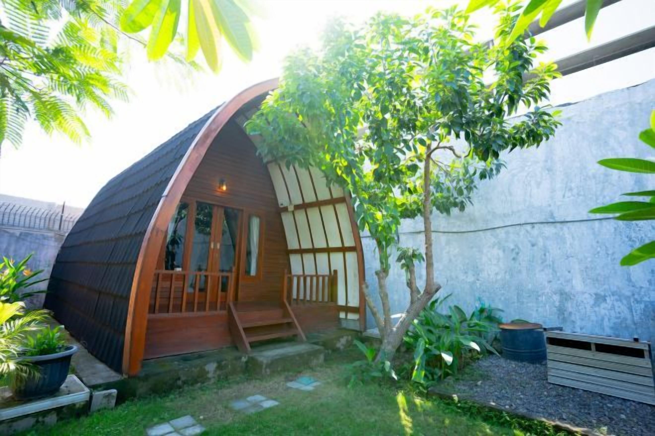 A dome-shaped structure with a wooden exterior, a small porch, and a garden area with plants and a tree.