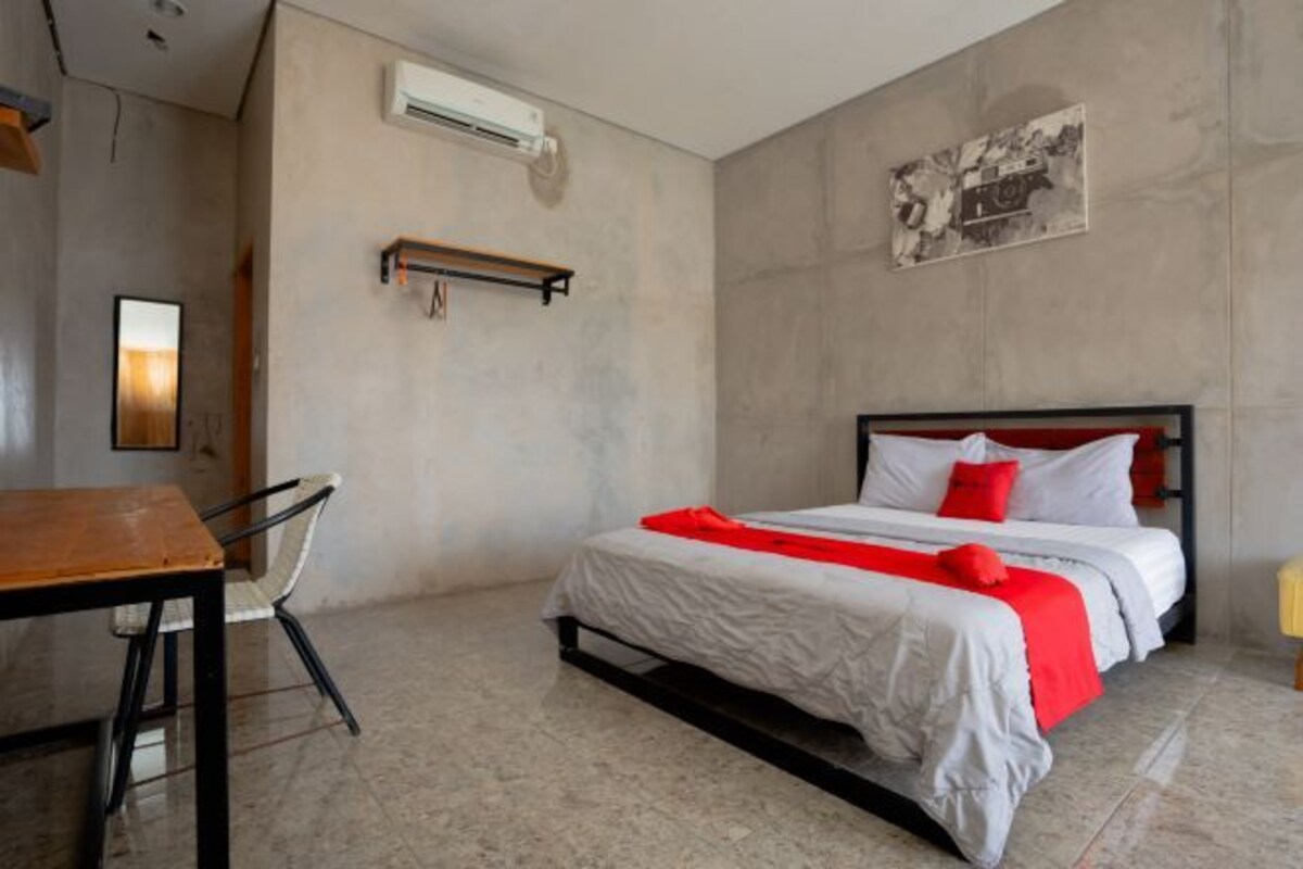 A hotel room with a bed, a desk, a chair, and a wall-mounted air conditioner.