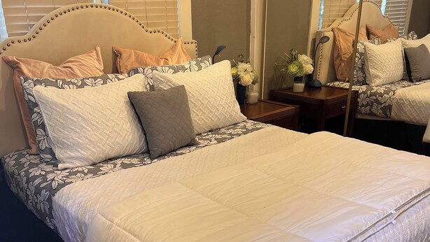 A neatly made bed with a quilted white comforter and a headboard with decorative nailhead trim.