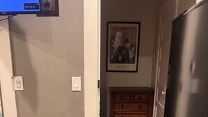 A kitchen with a refrigerator, a bench, wooden cabinets, and a painting on the wall.