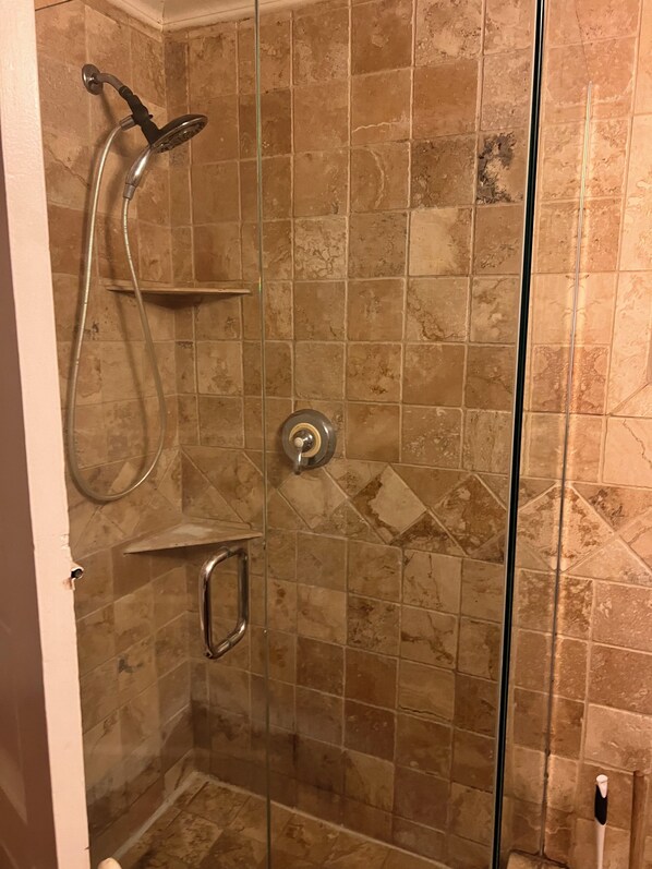 Een douchecabine met glazen wanden, een handdouche, een wandplankje en een bedieningspaneel voor de douche.