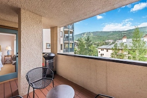 Een balkon met een grill, een stoel en uitzicht op een woonwijk met huizen en heuvels.