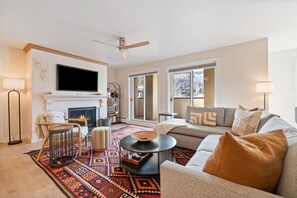 A modern living room with a fireplace, a large flat-screen TV, a sofa, and a patterned rug. - Beaver Creek Residences 2 Bedroom Luxury Vacation Rental (Avon)