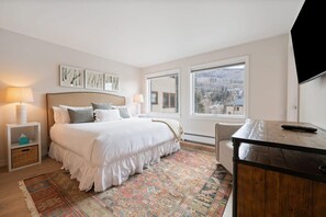 Una camera da letto con un letto grande, lampade sui comodini, una scrivania in legno, una televisione e vista su un paesaggio innevato dalla finestra.