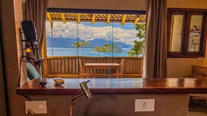 A bathroom with a large bowl sink, a faucet, a soap dispenser, and a window with a view of the ocean. - Casa Varandas (Ubatuba)