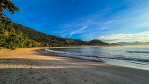 A beach with clear skies, sandy shore, and lush greenery. - Casa Varandas (Ubatuba)