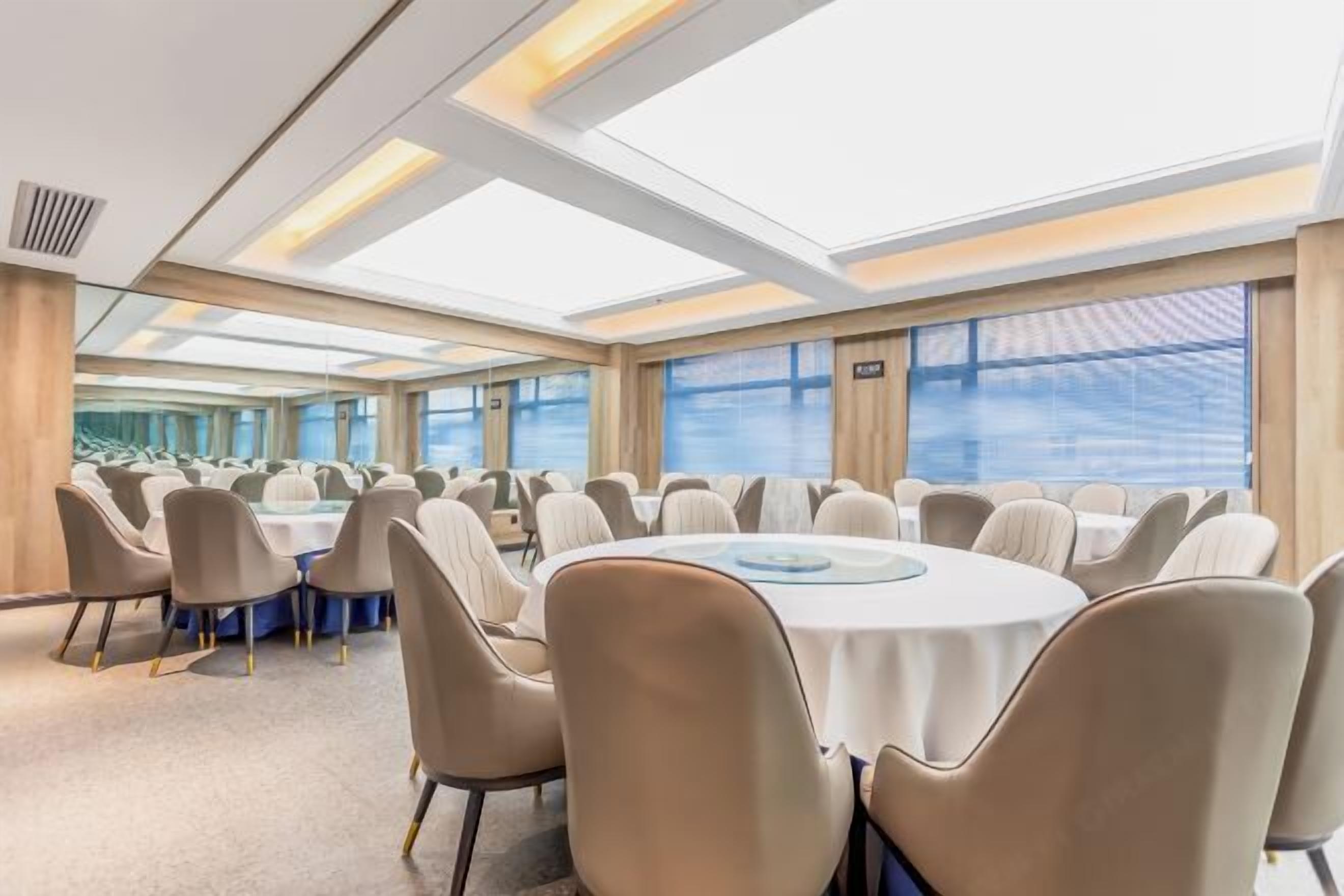 Een vergaderzaal met ronde tafels en stoelen, grote ramen en een hoge plafond met dakramen.