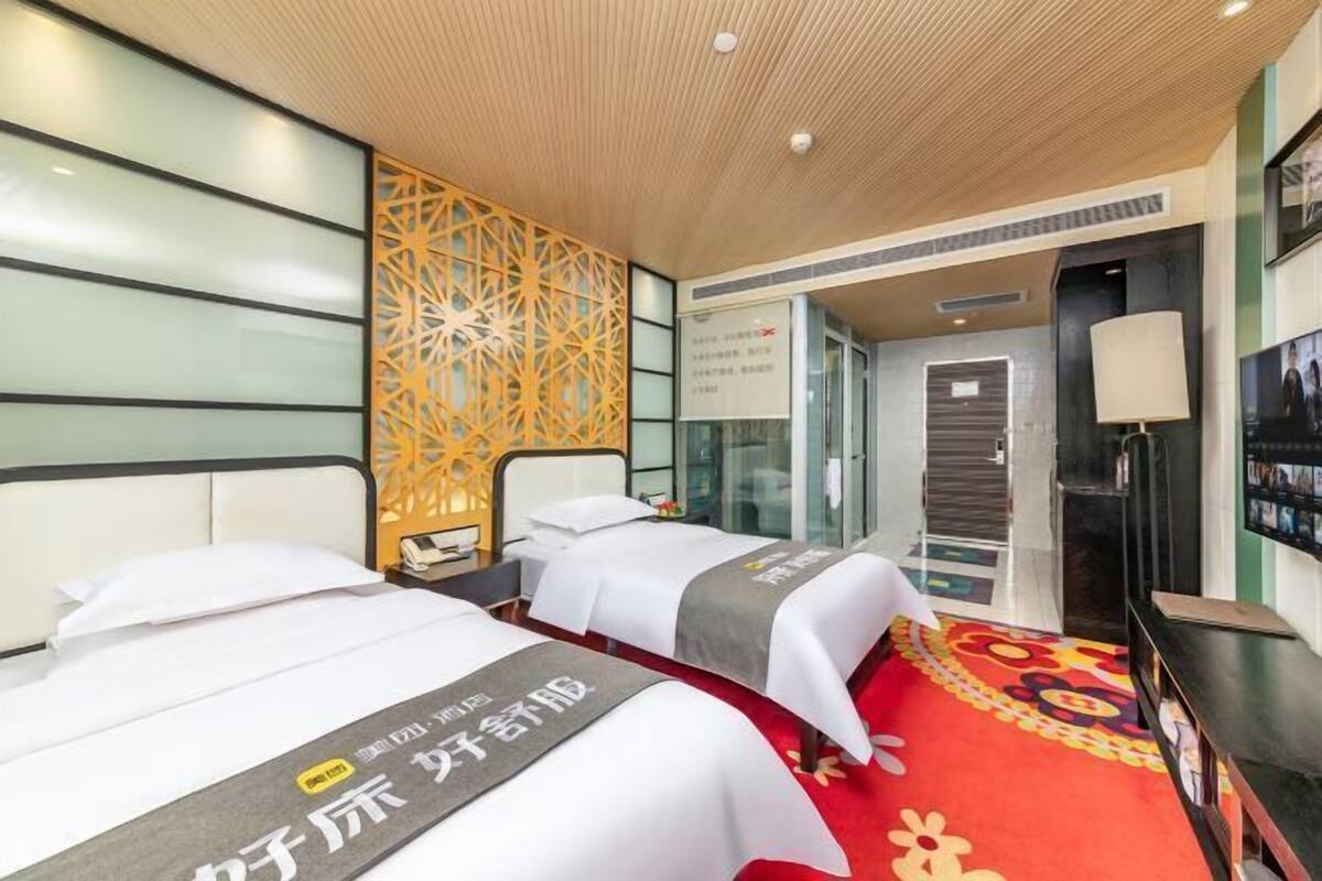 A hotel room with two beds, a red carpet, a decorative wall, and a modern ceiling design.