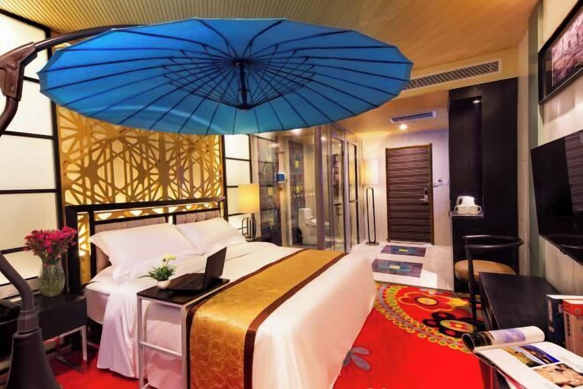 A hotel room with a bed, a desk, a laptop, a blue umbrella, and a red carpet.
