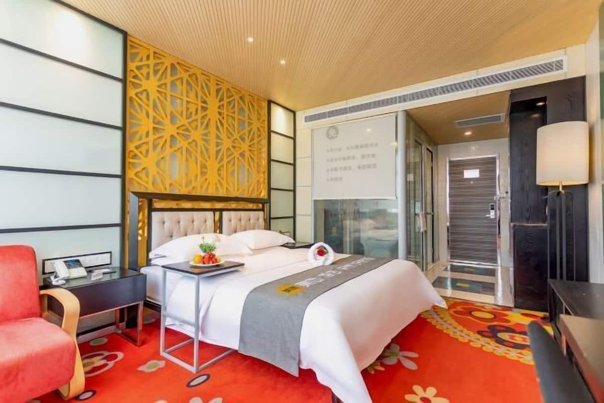 A hotel room with a bed, bedside table, chair, and a decorative wall panel.