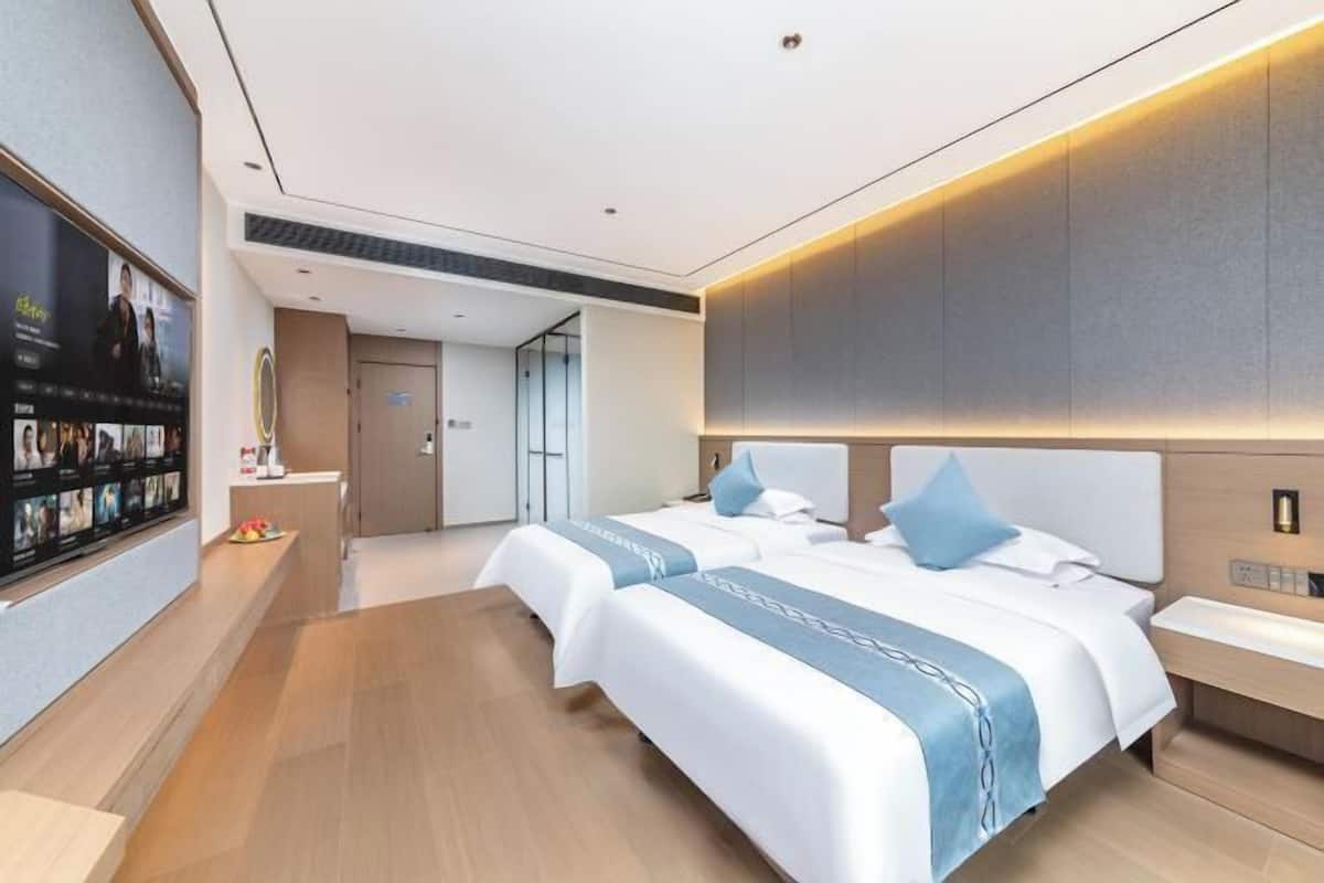 A modern hotel room with two beds, a large flat-screen TV, and a wooden floor.