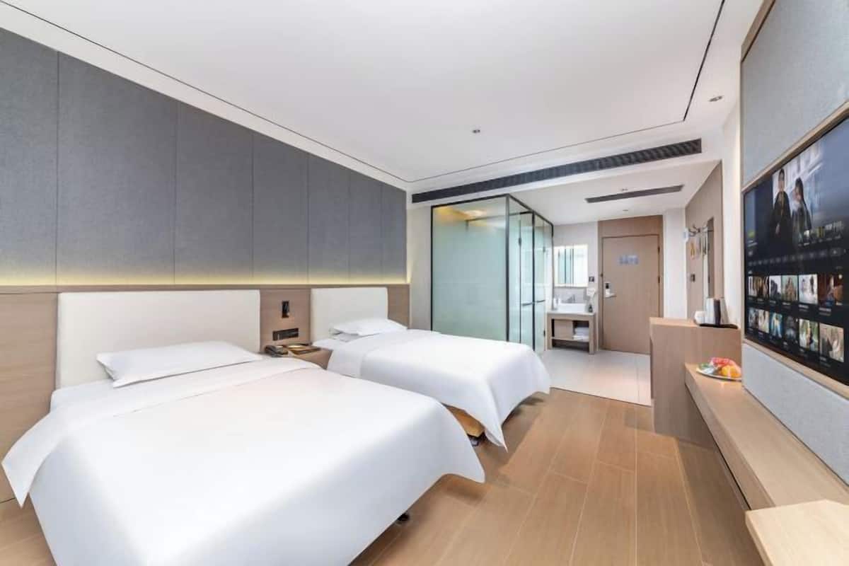 A modern hotel room with two beds, a small desk, a mirror, and a television on the wall.