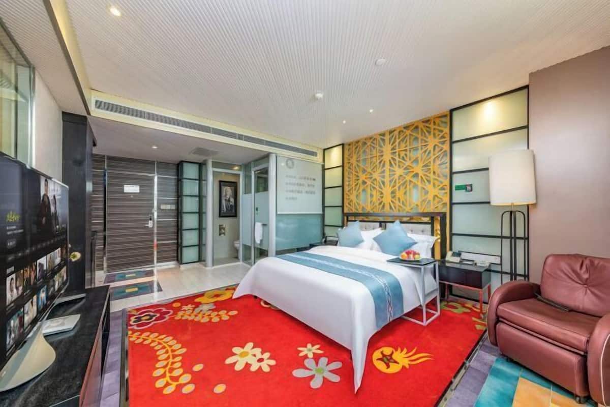 A hotel room with a bed, a red floral rug, a leather sofa, and a TV.