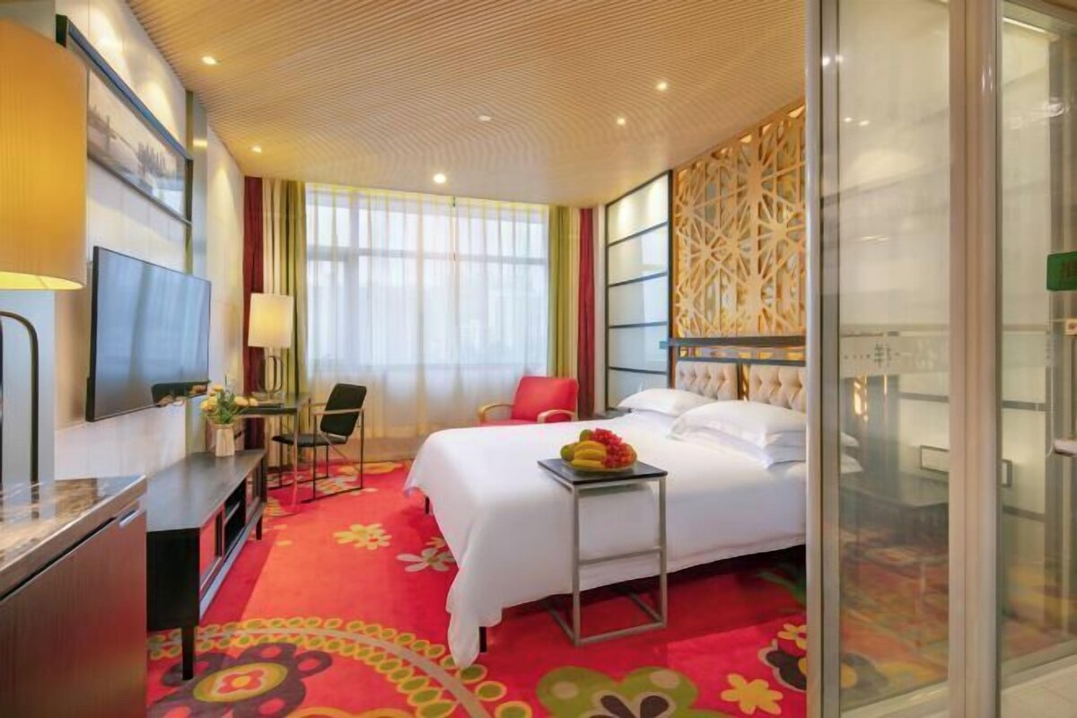 A hotel room with a bed, a desk with a TV, a chair, and a decorative wall panel.