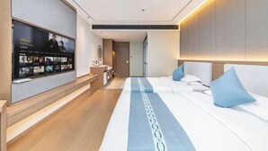A modern hotel room with a large flat-screen TV mounted on the wall, a bed with white bedding and blue pillows, and a wooden floor. - AutobotsOutbots Hotel (Aquarium Station) (Zhengzhou)