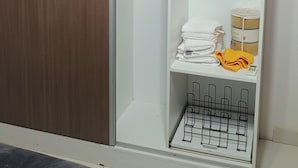 Une chambre avec une armoire, un lit et une étagère où sont pliés des vêtements et où est posée une serviette jaune.