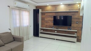 Un salon moderne avec un téléviseur à écran plat fixé à un mur en bois, un canapé beige et un rideau blanc.