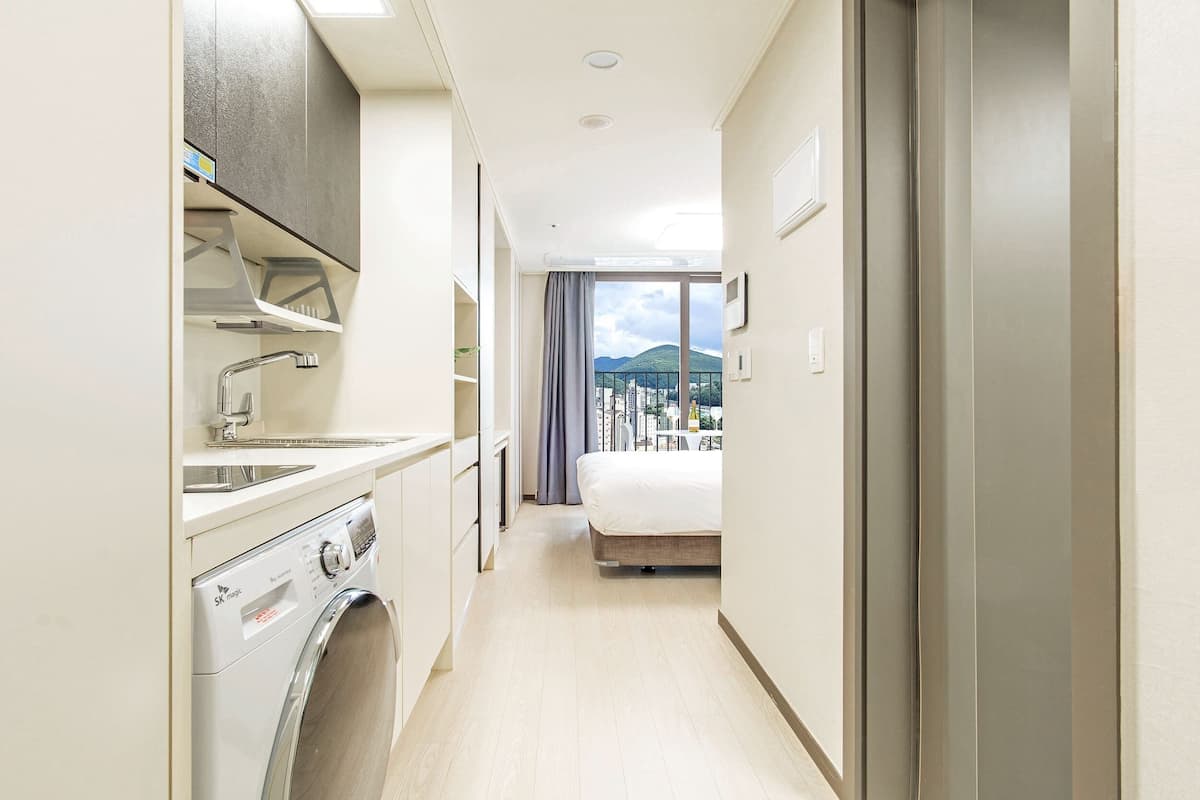Ett hotellrum med tvättmaskin, en säng, en balkong med utsikt över staden och ett stort fönster.